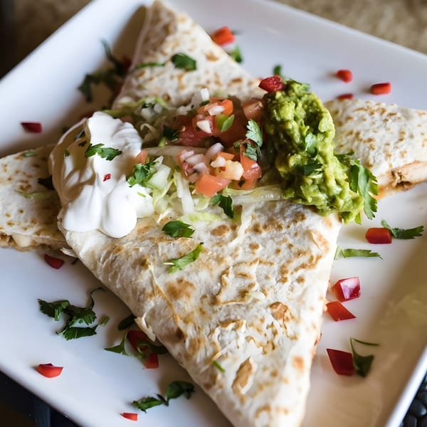 Refried Beans' quesadilla with guacamole, sour cream, pico de gallo, and lettuce on a white plate.