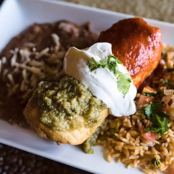 A Mexican dish with a chile relleno, refried beans, rice, and a dollop of sour cream.