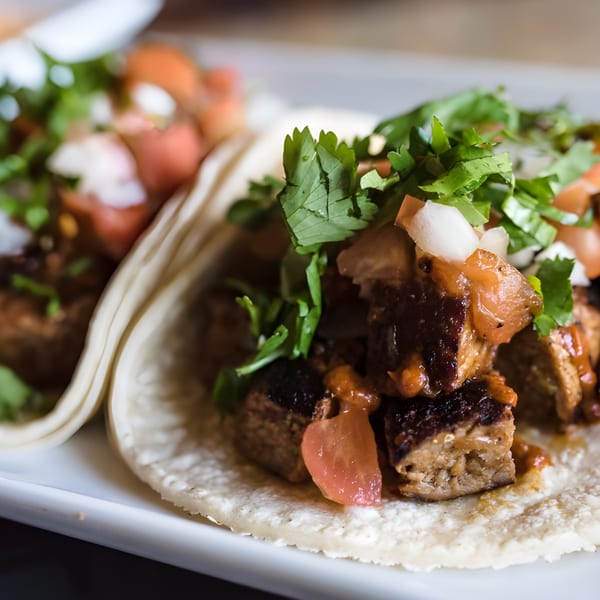 Two Refried Beans tacos with meat, salsa, cilantro, and onions on a white plate.